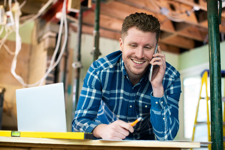 Man on phone next to a laptop in a building under construction. Photo by iStock.