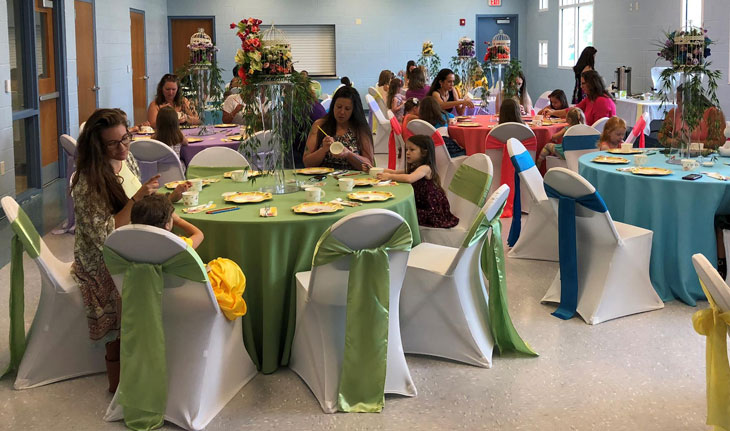 An event room set up with decorated tables and chairs inside Wickham Park Community Center with people enjoying the event.