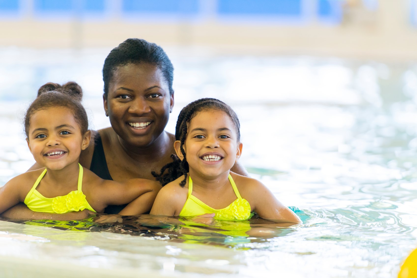 Mom holding two girls in a pool, all are smiling. Photo by Pool Safely/CPSC.