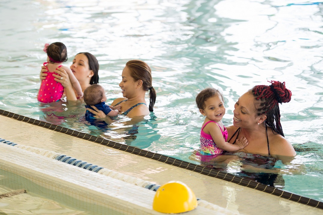 Three moms each holding one small baby in a pool getting ready to teach them to swim/be safe in the water. Photo by Pool Safely/CPSC.