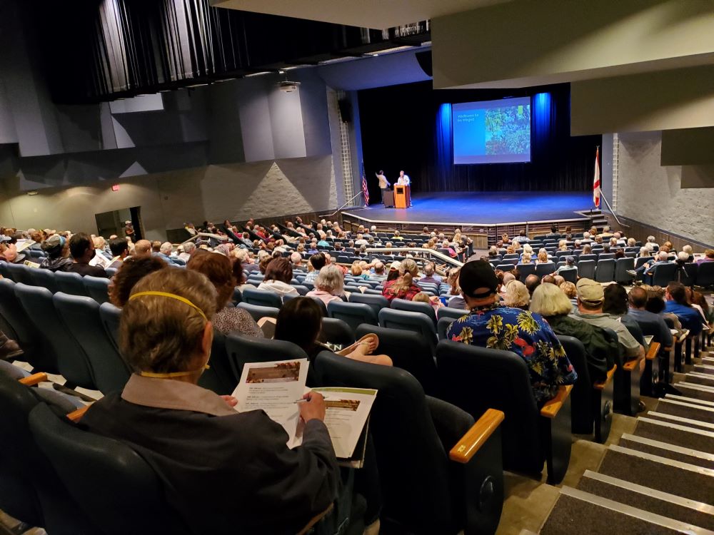 An audience in the Eau Gallie High School Auditorium watches a man give a presentation on stage.