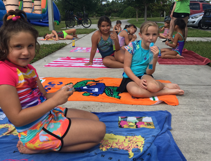 Kids sitting on towels eating ice pops.