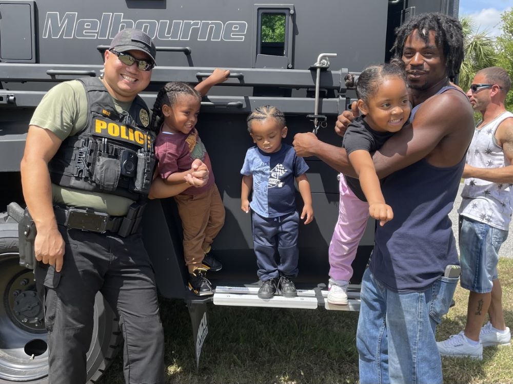 A police officer, three kids, and their dad stand in front of a BearCat vehicle