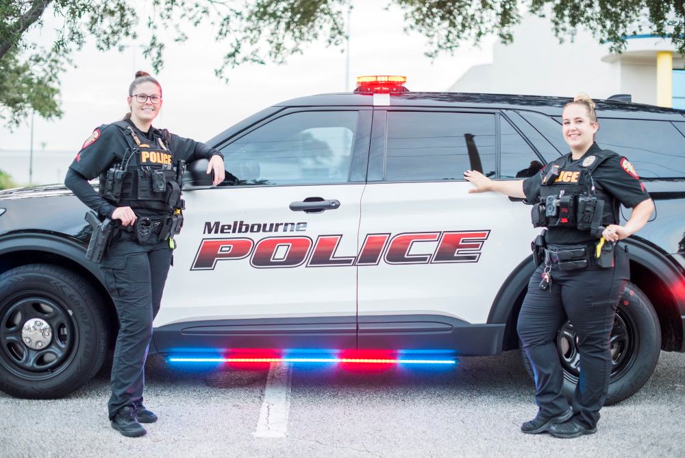 Two female officers standing in front of a police vehicle.