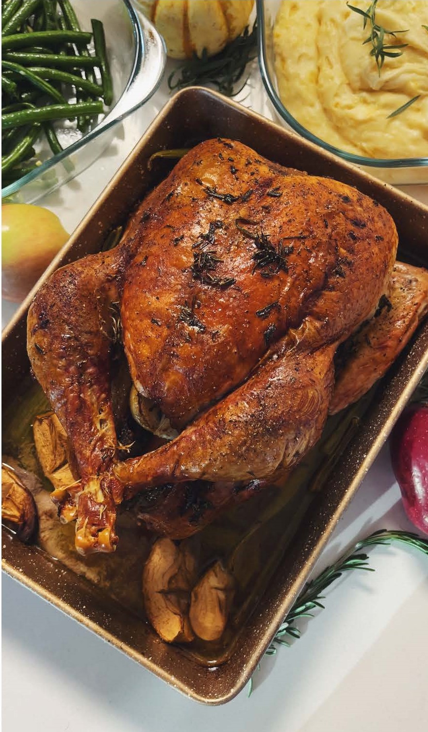 Cooked turkey in a pan next to a bowl of cooked green beans and a bowl of cooked mashed potatoes