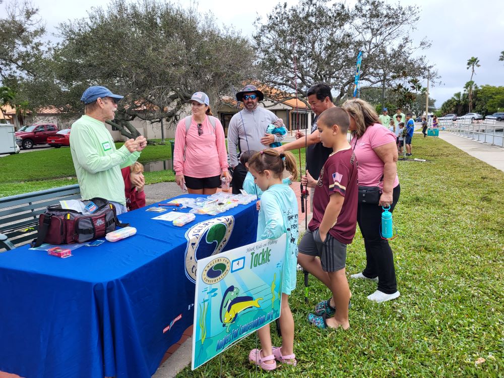 A man teaches fishing to a group of kids and adults at Indian River Lagoon Day, Front Street Park.