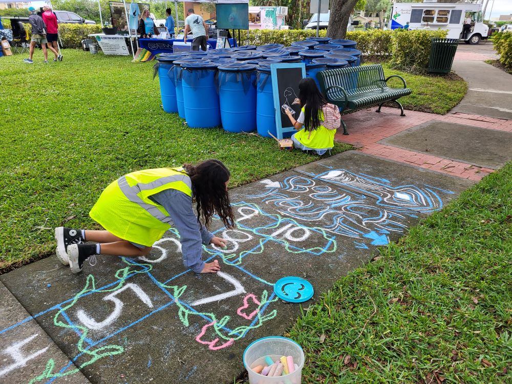 Two girls draw on the sidewalk with chalk at Indian River Lagoon Day, Front Street Park.