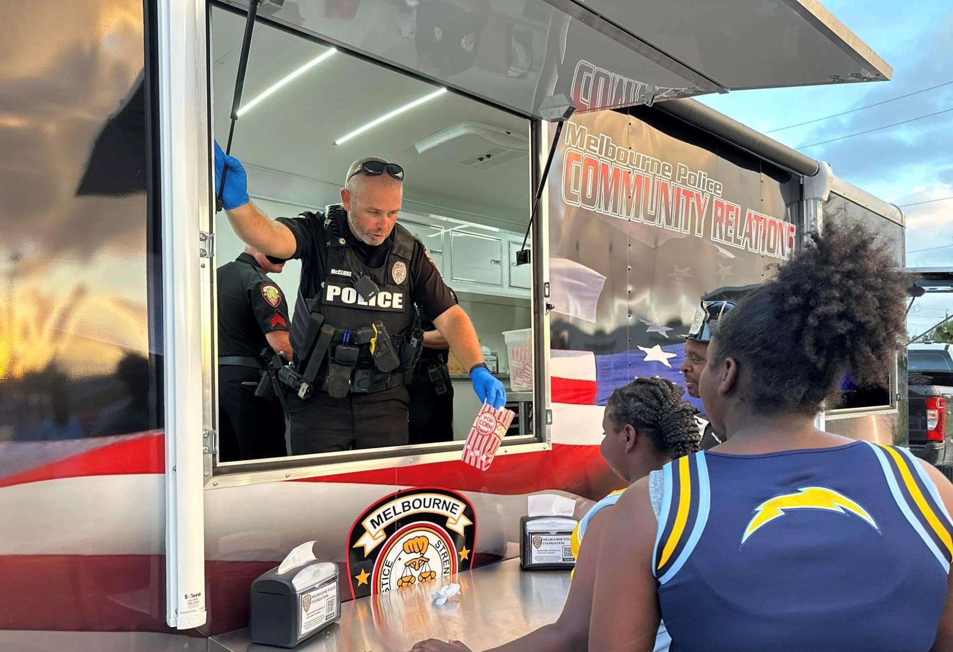 Police officer hands a bag of popcorn to a child from the Community Services Concessions Trailer.