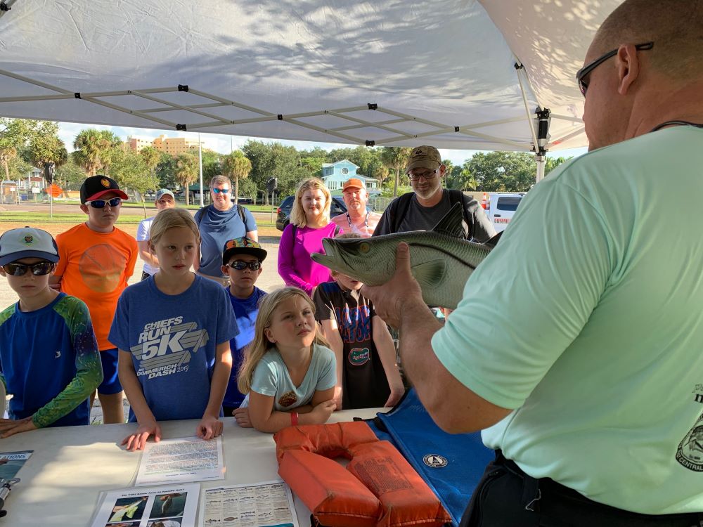 An officer explains fishing to a group of kids a the Kids Fishing Clinic.