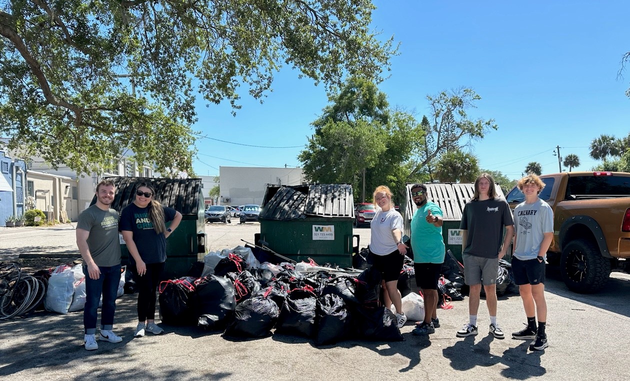 Group of Trash Bash volunteers in front of dumpsters with several filled trash bags.