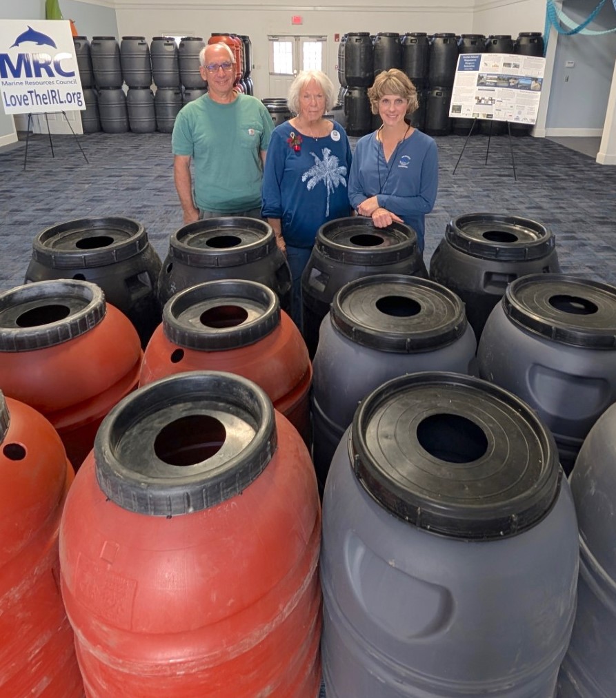 Three volunteers standing behind three rows of four rain barrels.