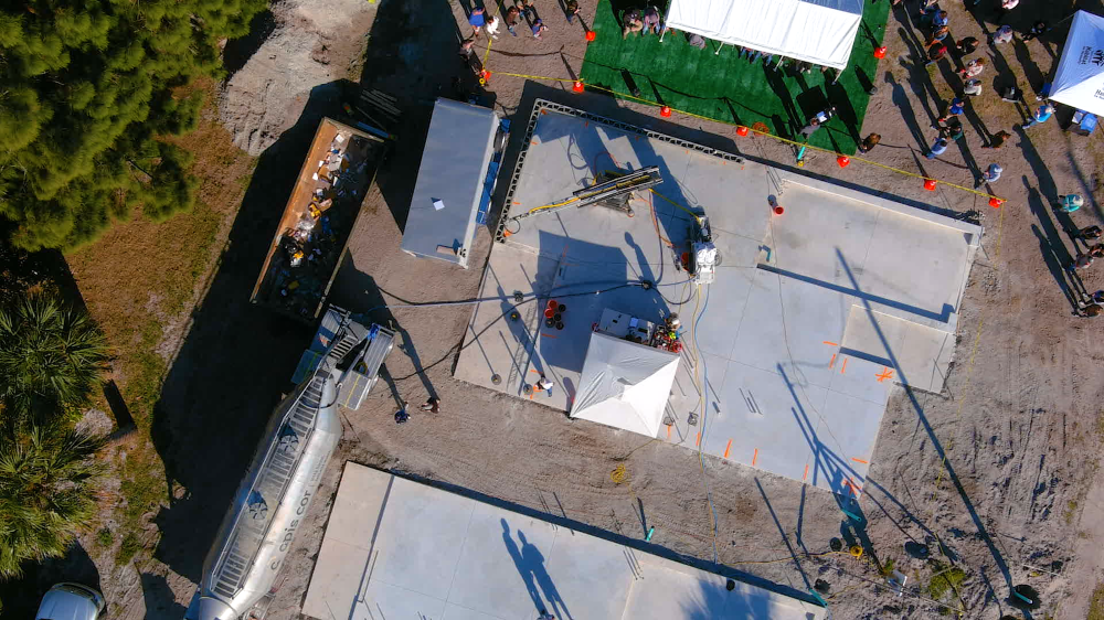 Aerial view of the wall of one home being built with 3D printing as attendees at the wall-raising ceremony watch